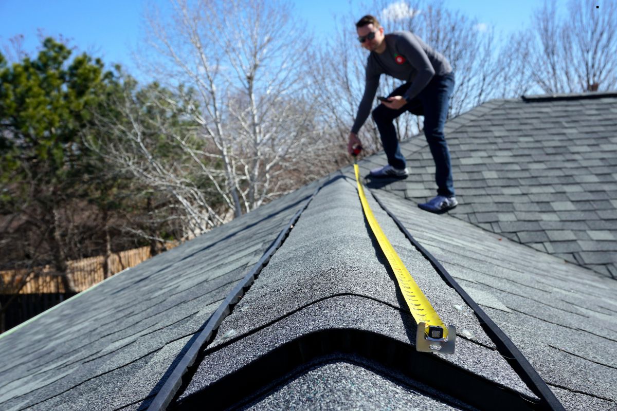 A man measuring the roof of a house, showcasing professional roofing services in action.